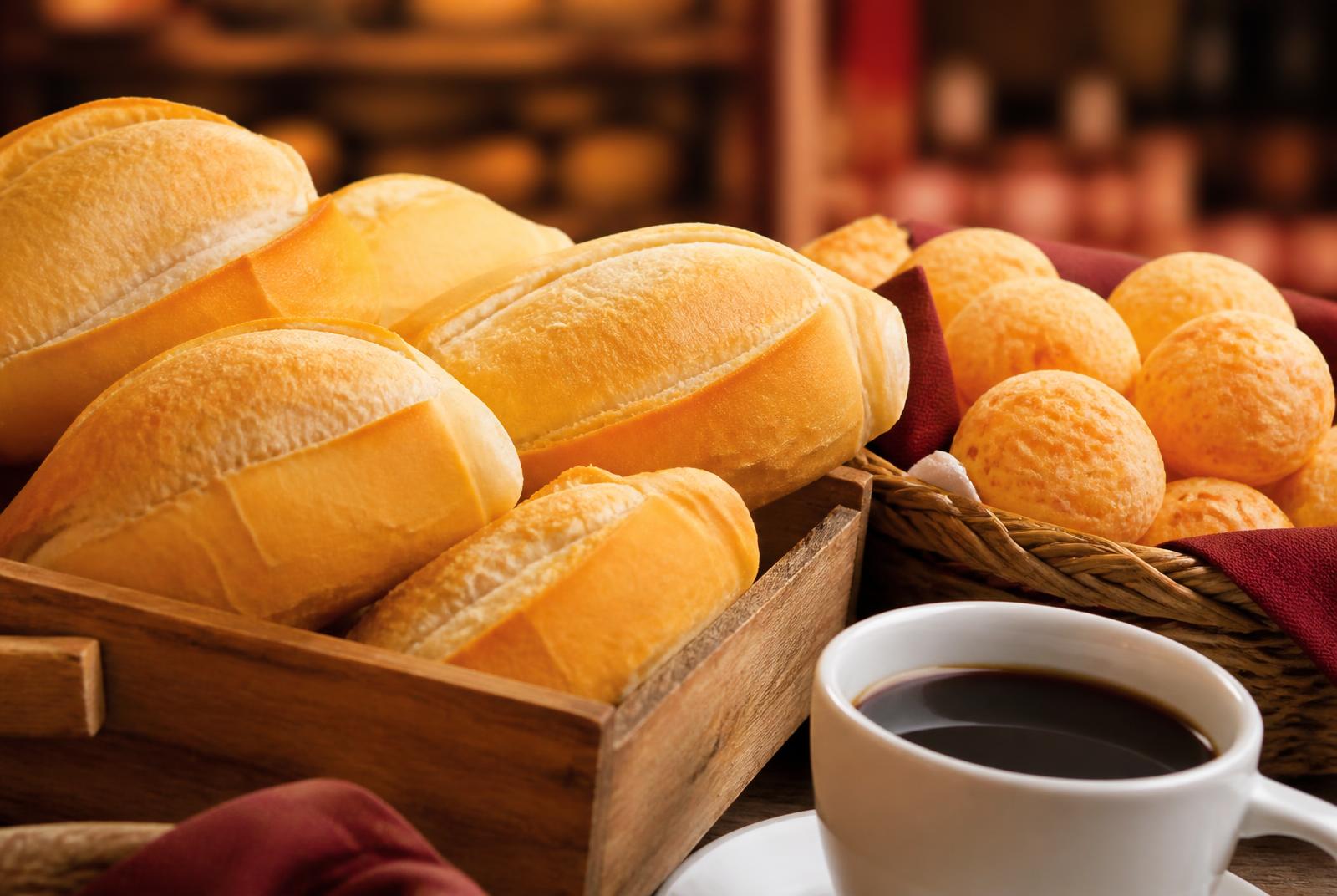 Pães franceses quentinhos em caixa de madeira, pães de queijo e uma xícara de café